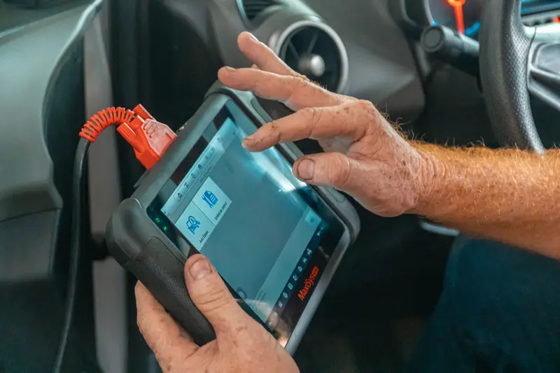 Ruke majstora na uređaju za kompjutersku dijagnostiku spojenom na auto